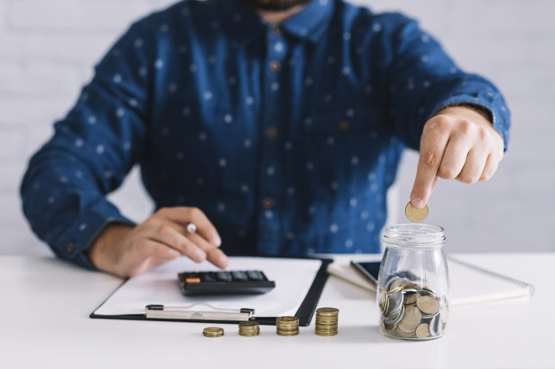 man putting coins in glass jar while using calculator